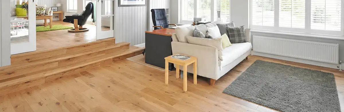 A modern living room with professionally installed laminate flooring, a beige sofa, a small side table, a gray rug, and large windows with white shutters in Reno, NV